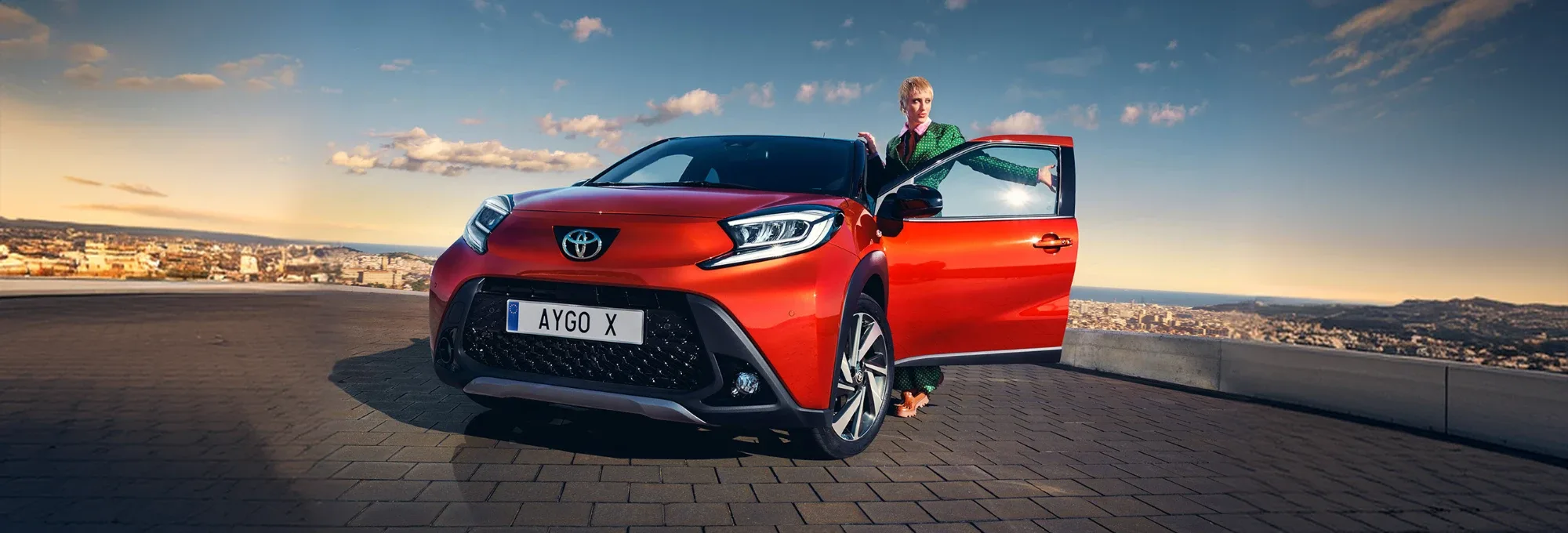 Toyota Aygo X rossa con una ragazza accanto alla portiera aperta